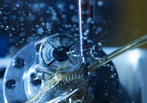 Lähikuva koneen työkalusta, jossa vesi roiskuu metalliosaan.