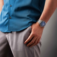 Mies, jolla on sininen paita ja harmaat housut ja ranteessa kello.