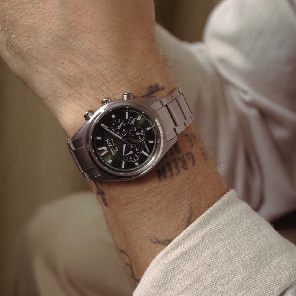 Mies käyttää hopeista Citizen Eco-Drive -kelloa vihreällä kellotaululla.