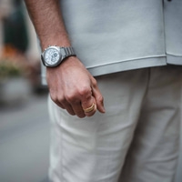 Mies, jolla on kello ja kultasormus, lähikuva hänen kädestään ja vaatteistaan.