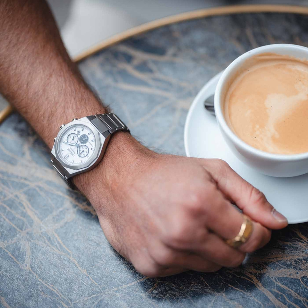 Lähikuva miehen rannekellosta ja kahvikupista pöydällä.