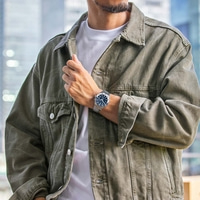 Mies, jolla on kello ja vihreä takki, poseeraa valokuvaa varten.