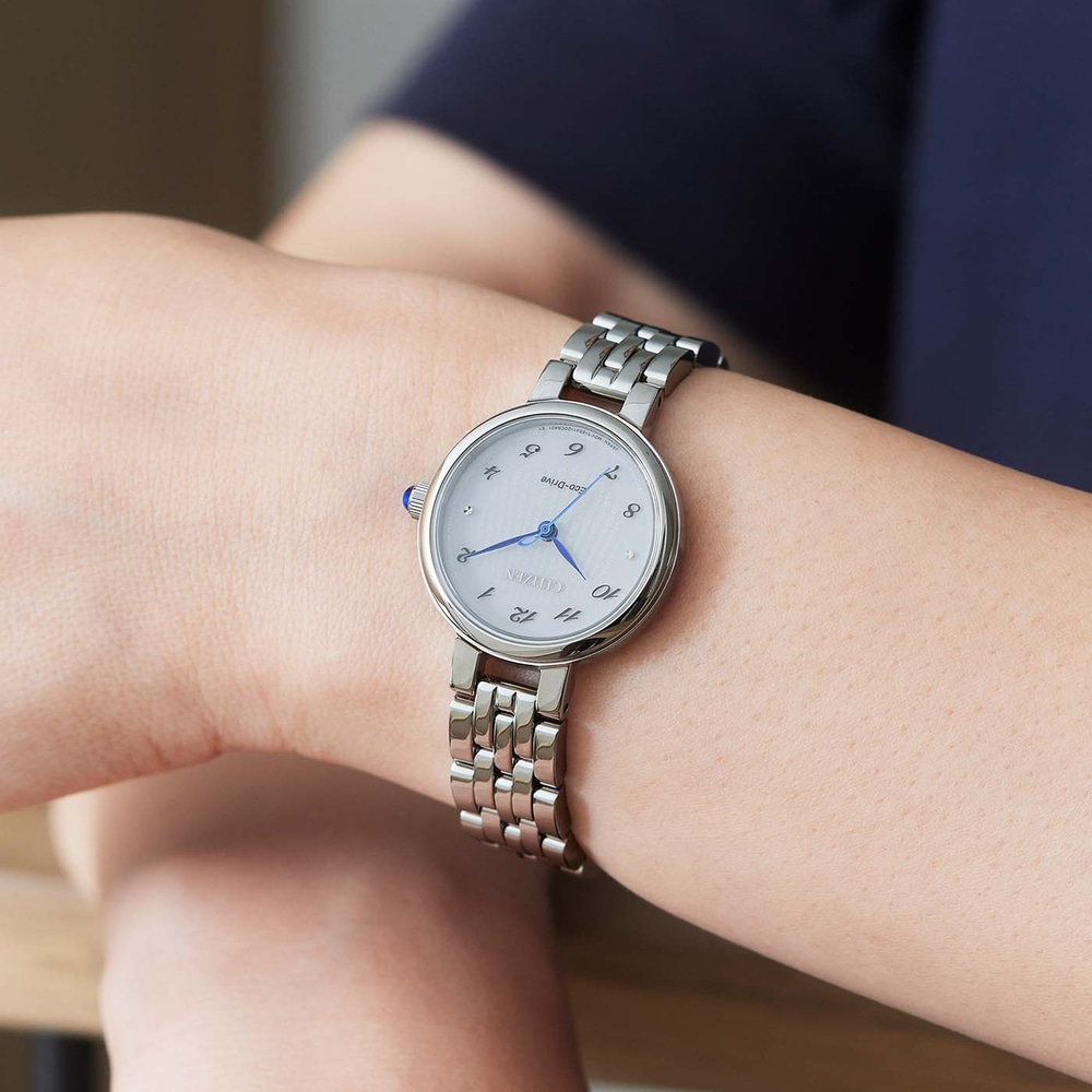 Citizen-kello ranteessa, hopeinen ranneke, valkoinen kellotaulu, siniset viisarit, tyylikäs muotoilu