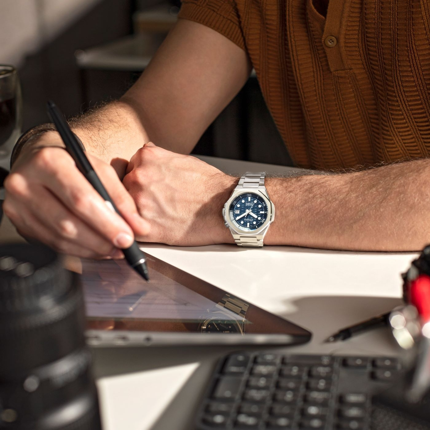 Mies työskentelee tabletilla, kello ranteessa ja kirjoittaa kynällä.